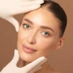 Doctor examining young woman's face over beige studio background.