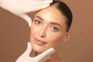 Doctor examining young woman's face over beige studio background.