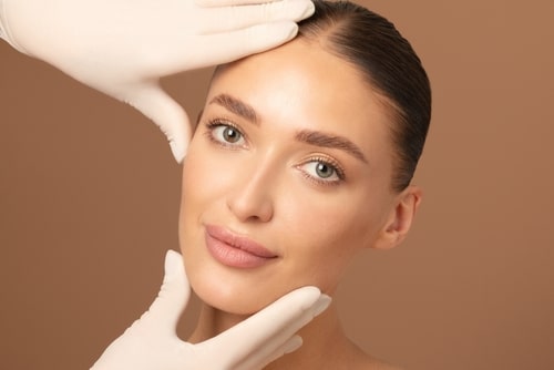 Doctor examining young woman's face over beige studio background.