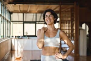 Smiling Latina woman indoors with sun coming through the windows. She’s wearing workout attire as part of her new healthy lifestyle