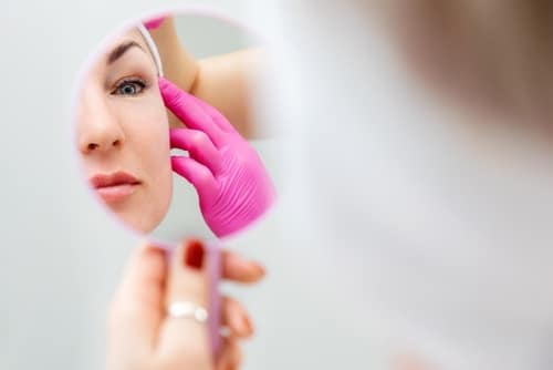 Woman looking in mirror being evaluated as a facelift candidate in Scottsdale, AZ