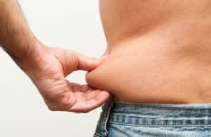 Man, wearing jeans, is shown from behind as he pinches extra skin and fat