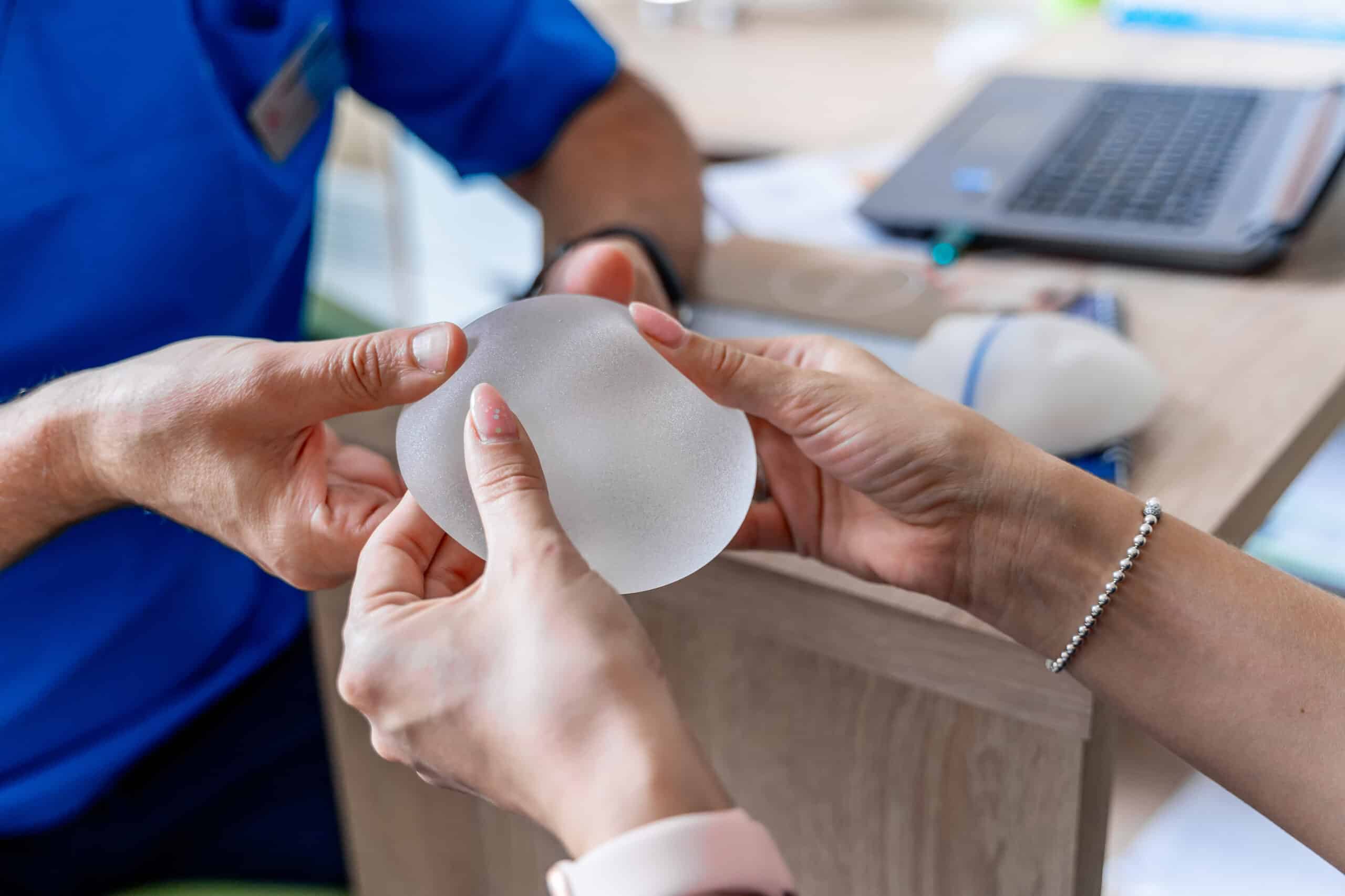 Doctors hands a woman a breast implant as he explains its type and benefits