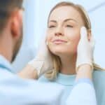Woman smiling as her surgeon examines her face before facial fat grafting surgery
