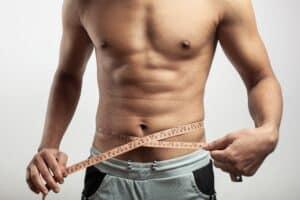 Muscular man measuring his waist with a tape measure, symbolizing liposuction results and body sculpting