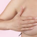 Woman holds one hand over her breast, with a black dotted line at the bottom of the breast before implant placement