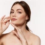 Youthful woman raises her hands, holding them close to her lower face after a mini facelift