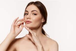 Youthful woman raises her hands, holding them close to her lower face after a mini facelift