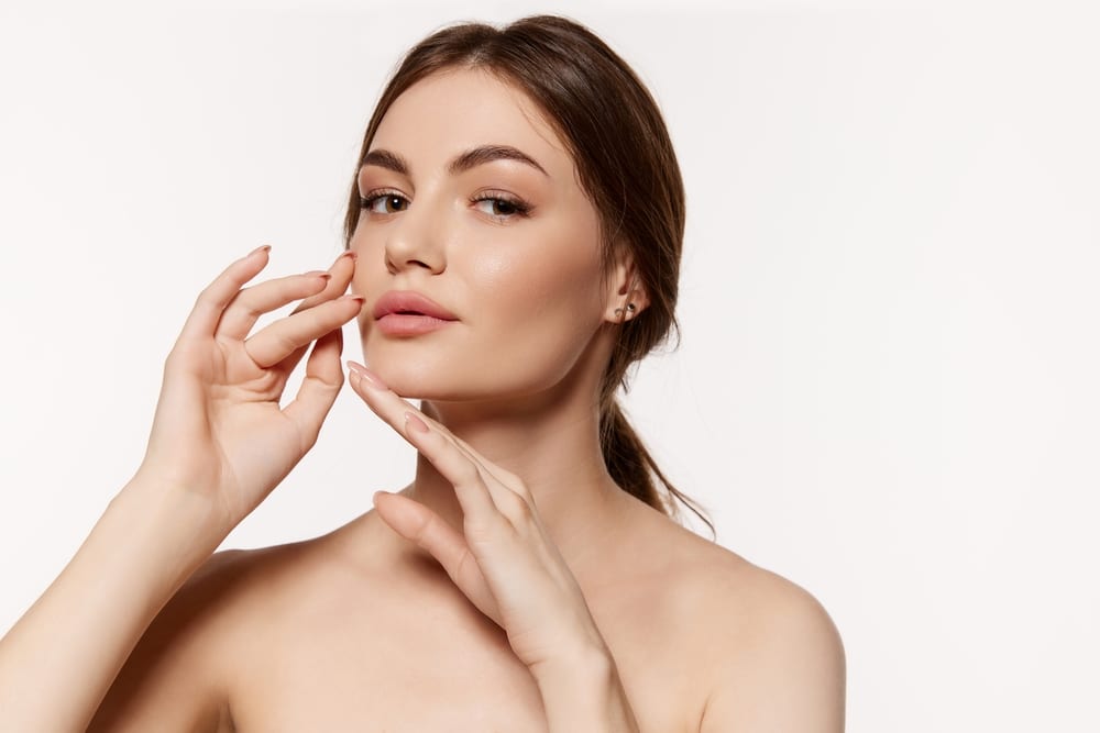 Youthful woman raises her hands, holding them close to her lower face after a mini facelift