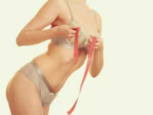 Woman measuring her chest with measuring tape while considering breast implant sizing and breast augmentation options.