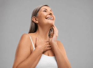 Smiling woman touching her neck and jawline after neck lift surgery for a smoother, more defined profile.