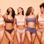 Five women with different body types and breast proportions smiling together, showing how breast size can complement each person’s frame and preferences.
