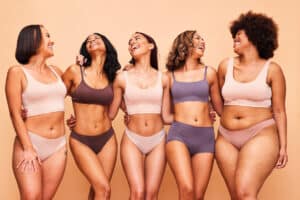 Five women with different body types and breast proportions smiling together, showing how breast size can complement each person’s frame and preferences.