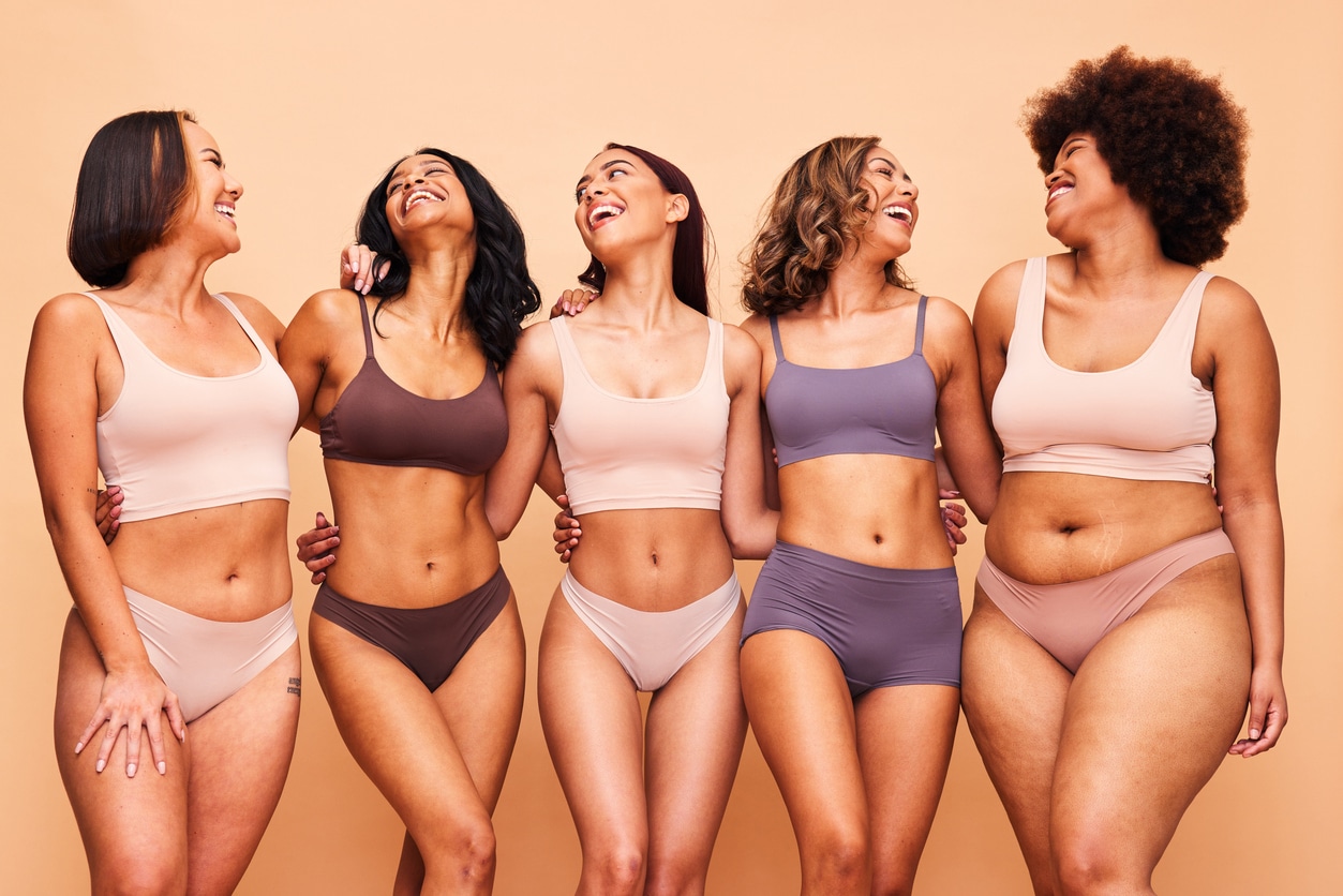 Five women with different body types and breast proportions smiling together, showing how breast size can complement each person’s frame and preferences.