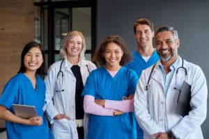 Group of doctors and medical professionals in scrubs and white coats standing together.