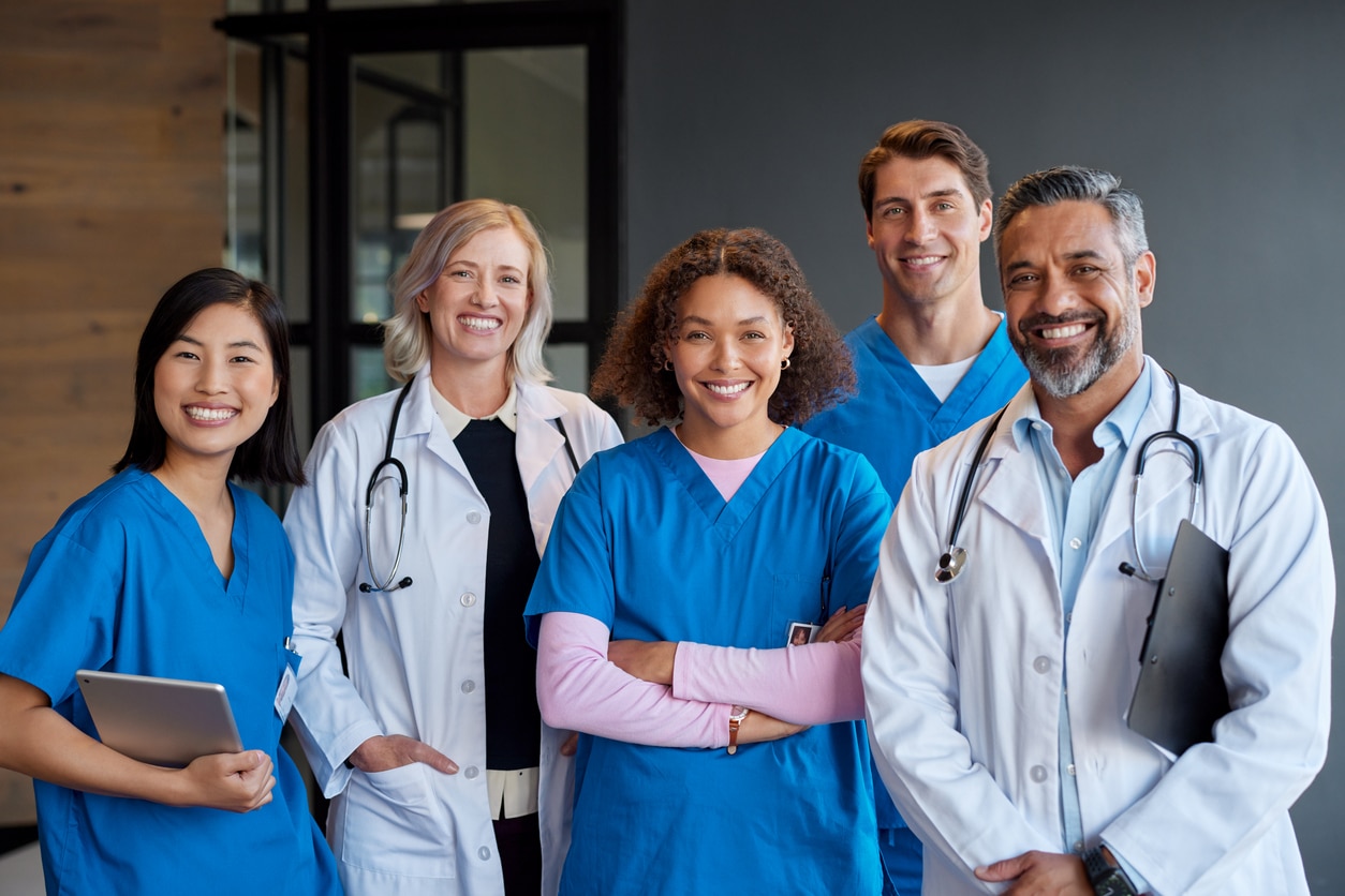 Group of doctors and medical professionals in scrubs and white coats standing together.